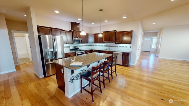 kitchen featuring a kitchen bar, stone countertops, appliances with stainless steel finishes, a kitchen island, and pendant lighting