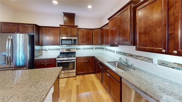 kitchen featuring sink, appliances with stainless steel finishes, light stone counters, tasteful backsplash, and light wood-type flooring