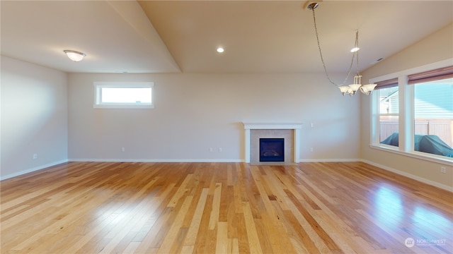 unfurnished living room featuring an inviting chandelier, lofted ceiling, a tile fireplace, and light hardwood / wood-style flooring