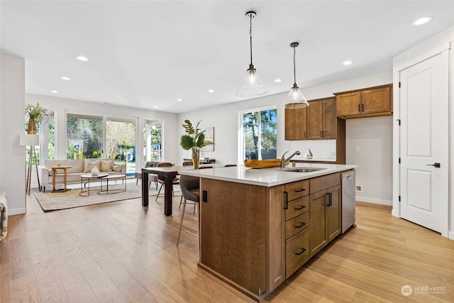 kitchen with sink, hanging light fixtures, stainless steel dishwasher, an island with sink, and light hardwood / wood-style floors