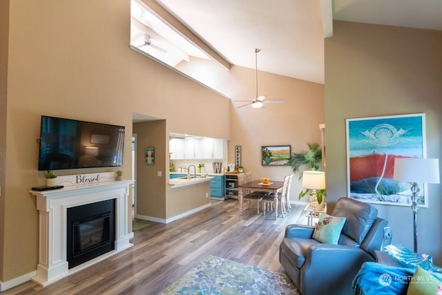 living room featuring sink, high vaulted ceiling, light wood-type flooring, beamed ceiling, and ceiling fan