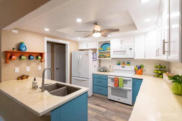 kitchen featuring sink, white appliances, blue cabinetry, white cabinets, and a raised ceiling