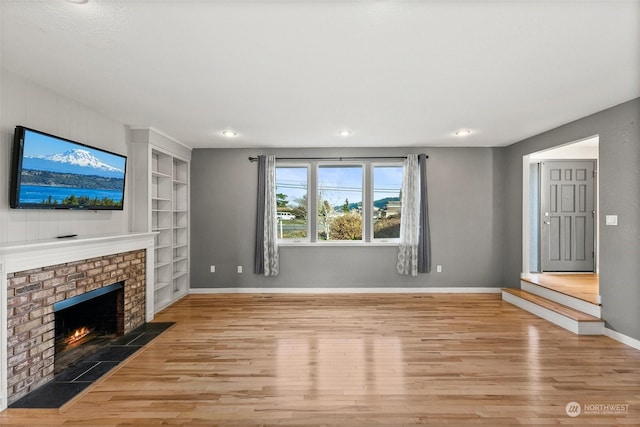 unfurnished living room featuring light hardwood / wood-style flooring, built in shelves, and a fireplace