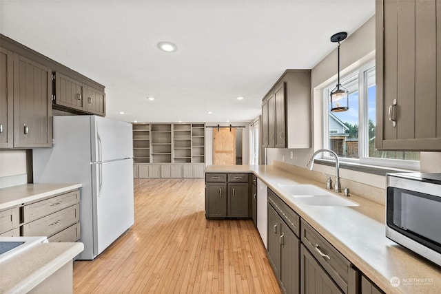 kitchen featuring decorative light fixtures, sink, dishwashing machine, white refrigerator, and light wood-type flooring