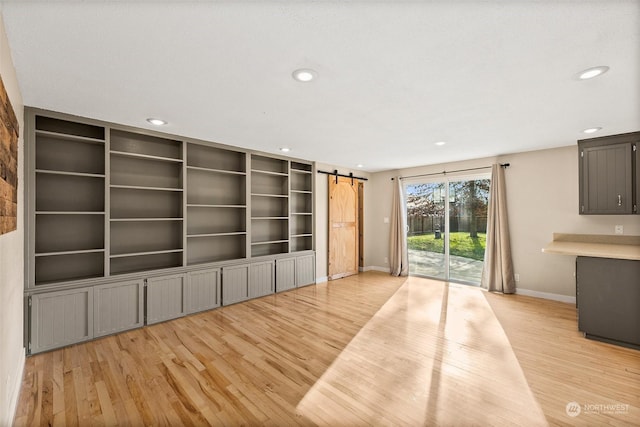 unfurnished living room featuring light hardwood / wood-style flooring, built in features, and a barn door