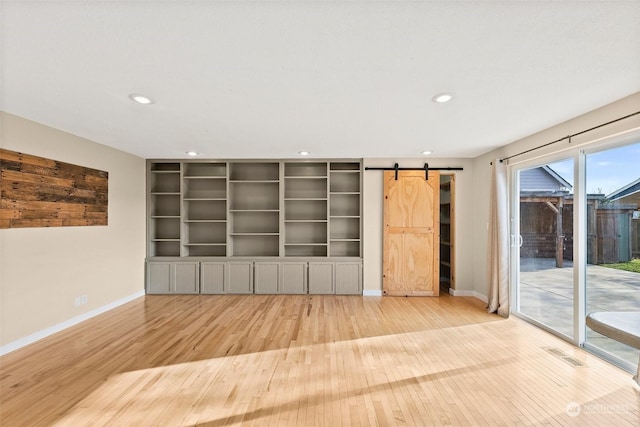 unfurnished living room featuring a barn door, built in features, and light wood-type flooring