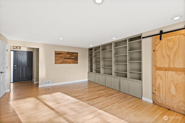 interior space with a barn door, light hardwood / wood-style flooring, and built in shelves