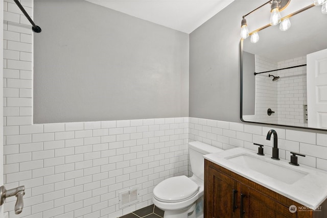 bathroom with a tile shower, tile walls, vanity, toilet, and tile patterned floors