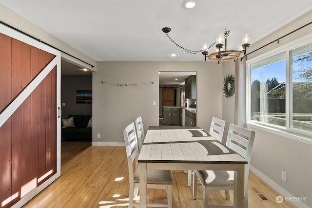 dining area with an inviting chandelier, light hardwood / wood-style floors, and a barn door