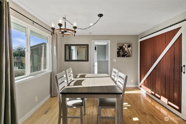 dining space featuring a barn door, light wood-type flooring, and a notable chandelier