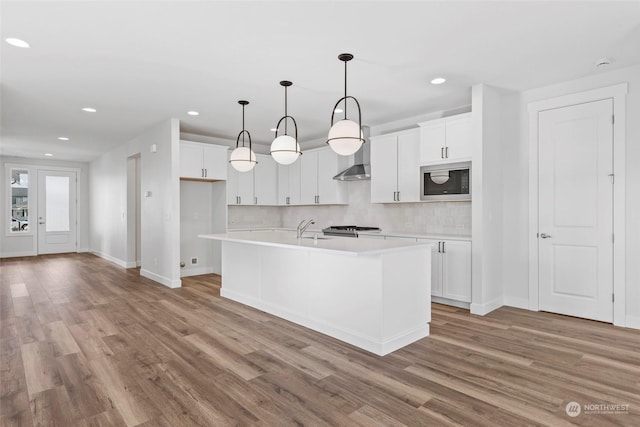 kitchen with built in microwave, tasteful backsplash, white cabinets, and a center island with sink