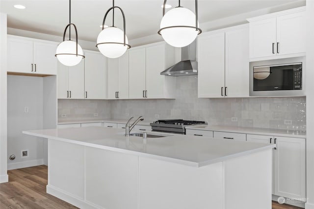 kitchen with pendant lighting, built in microwave, sink, white cabinets, and a kitchen island with sink