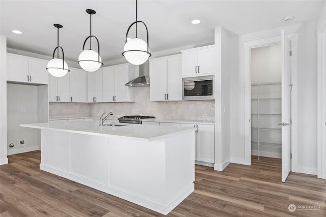 kitchen with sink, white cabinetry, black microwave, a kitchen island with sink, and backsplash