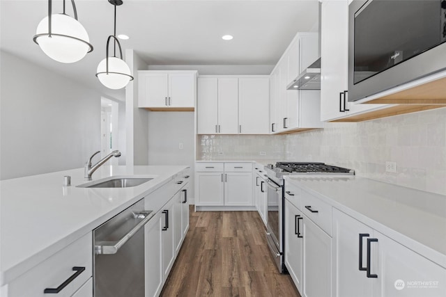 kitchen with stainless steel appliances, white cabinetry, hanging light fixtures, and wall chimney range hood