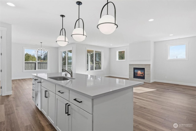 kitchen with sink, hanging light fixtures, light wood-type flooring, a center island with sink, and white cabinets