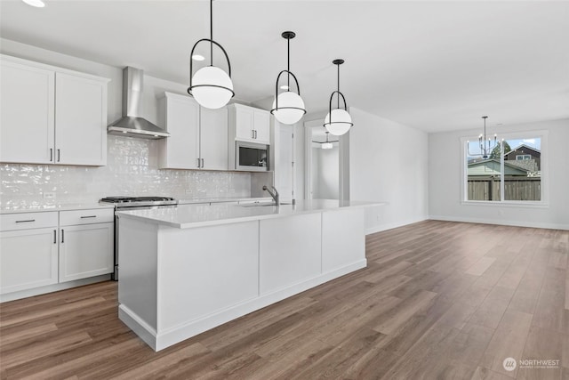 kitchen with white cabinetry, sink, hanging light fixtures, and wall chimney range hood