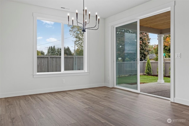 unfurnished dining area with hardwood / wood-style floors, a wealth of natural light, and a notable chandelier