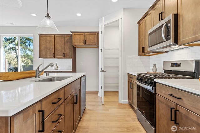 7157 91st St E, Puyallup, WA 98371 - kitchen with appliances with stainless steel finishes, a sink, light wood-style floors, pendant lighting, and tasteful backsplash
