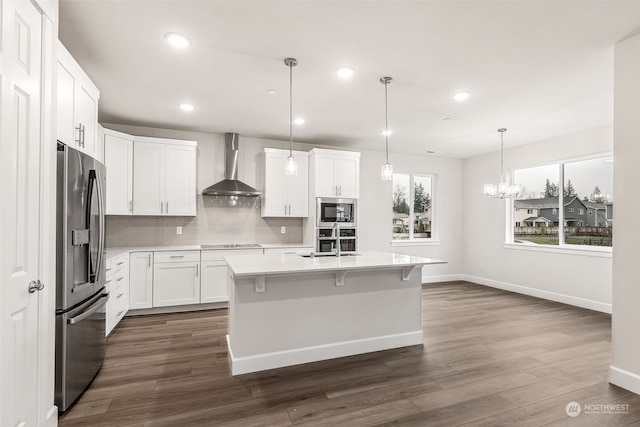 kitchen featuring hanging light fixtures, white cabinetry, appliances with stainless steel finishes, and wall chimney exhaust hood