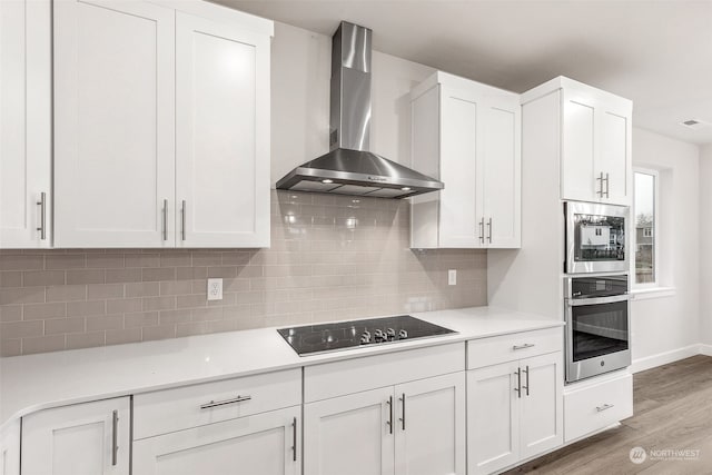 kitchen featuring wall chimney exhaust hood, white cabinets, stainless steel appliances, light hardwood / wood-style floors, and backsplash