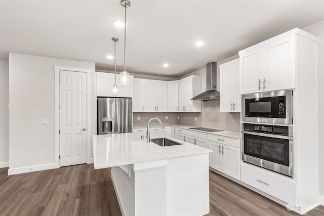 kitchen featuring sink, a center island with sink, hanging light fixtures, stainless steel appliances, and wall chimney range hood