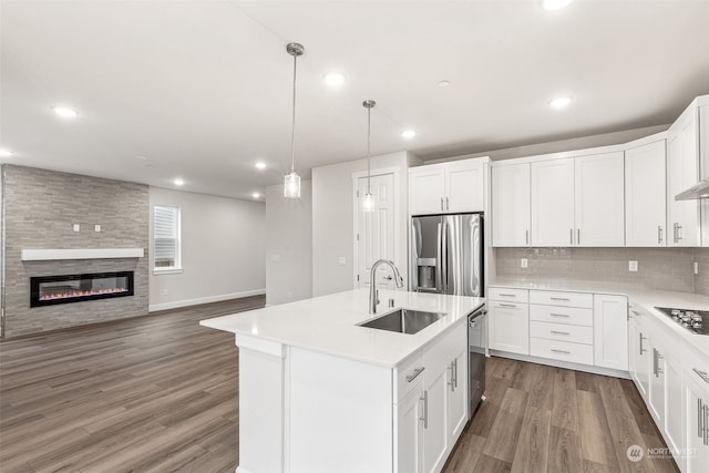 kitchen with appliances with stainless steel finishes, a fireplace, an island with sink, sink, and white cabinets