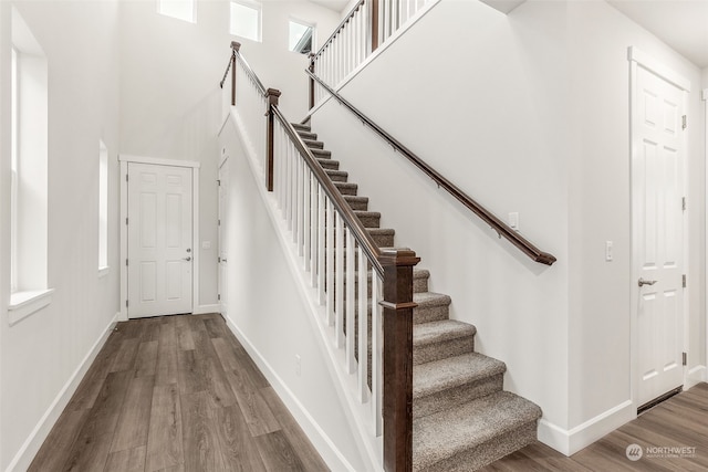 stairs with hardwood / wood-style flooring and a towering ceiling