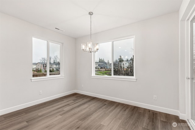 unfurnished dining area featuring an inviting chandelier and wood-type flooring