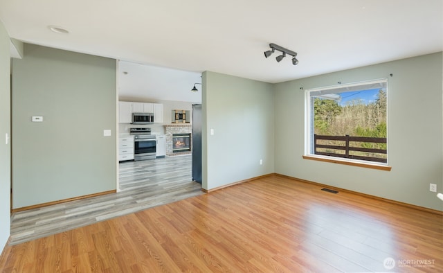 unfurnished living room featuring light wood-type flooring, visible vents, rail lighting, baseboards, and a brick fireplace