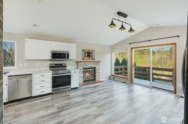 kitchen with light wood finished floors, stainless steel appliances, light countertops, vaulted ceiling, and white cabinetry