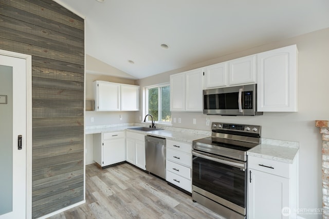 kitchen featuring a sink, white cabinetry, appliances with stainless steel finishes, light wood finished floors, and vaulted ceiling