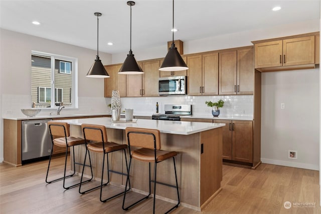 kitchen with sink, a kitchen island, pendant lighting, stainless steel appliances, and light hardwood / wood-style floors