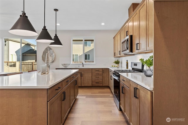 kitchen featuring appliances with stainless steel finishes, decorative light fixtures, sink, decorative backsplash, and light wood-type flooring