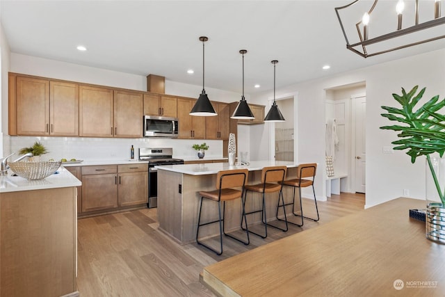 kitchen featuring an island with sink, appliances with stainless steel finishes, pendant lighting, and light hardwood / wood-style floors