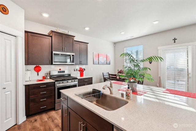 kitchen featuring sink, dark brown cabinets, stainless steel appliances, light hardwood / wood-style floors, and decorative backsplash