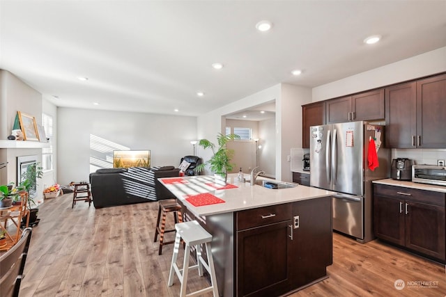 kitchen with a kitchen bar, dark brown cabinetry, sink, stainless steel fridge, and an island with sink