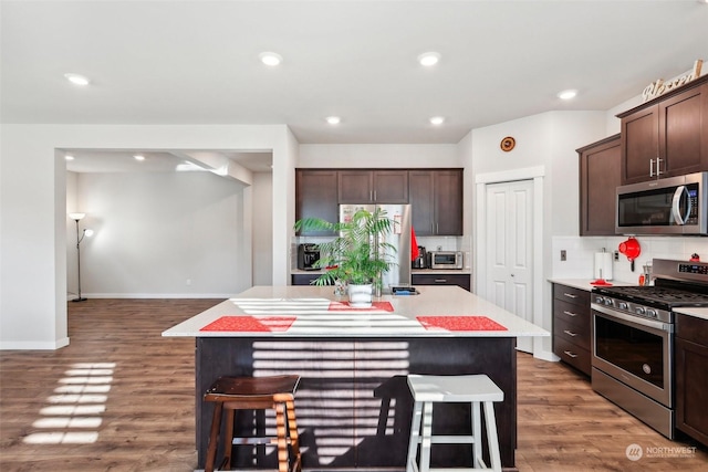 kitchen with a kitchen bar, dark brown cabinets, a center island, and appliances with stainless steel finishes