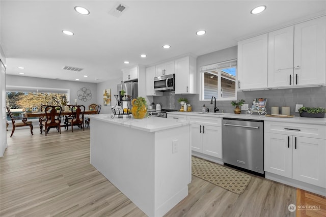 kitchen featuring sink, appliances with stainless steel finishes, white cabinetry, a center island, and light wood-type flooring