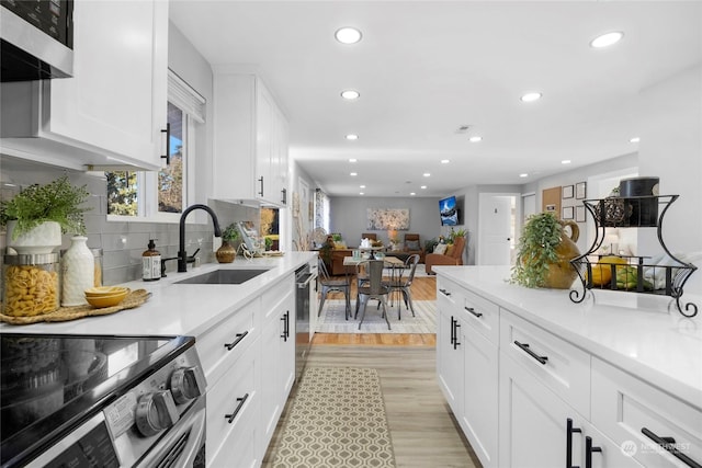 kitchen with sink, white cabinetry, light hardwood / wood-style flooring, appliances with stainless steel finishes, and decorative backsplash