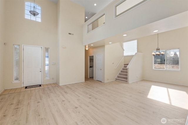 foyer entrance featuring an inviting chandelier, light wood-style flooring, stairs, and plenty of natural light