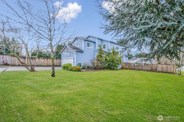 view of yard with driveway, an attached garage, and fence