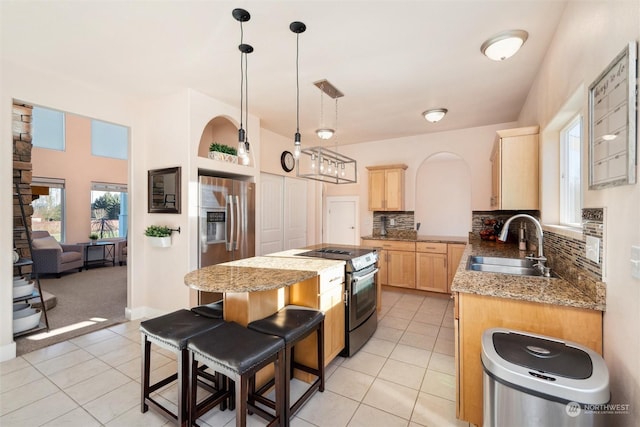 kitchen with pendant lighting, sink, appliances with stainless steel finishes, a center island, and light brown cabinets