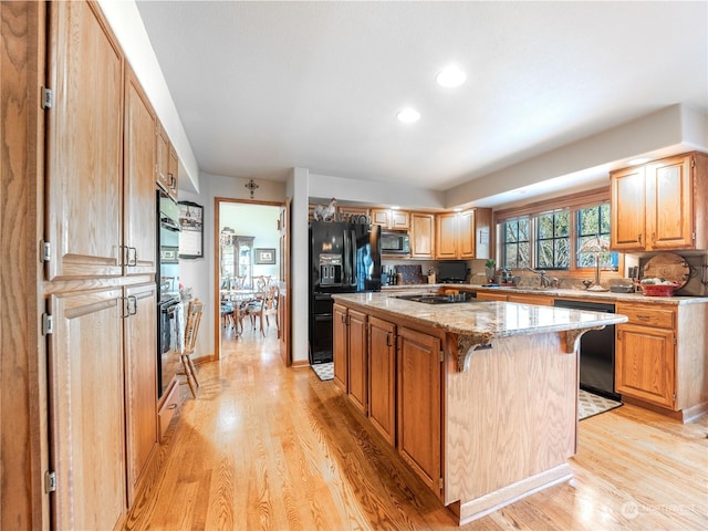 kitchen with a breakfast bar, light stone countertops, black appliances, a kitchen island, and light wood-type flooring