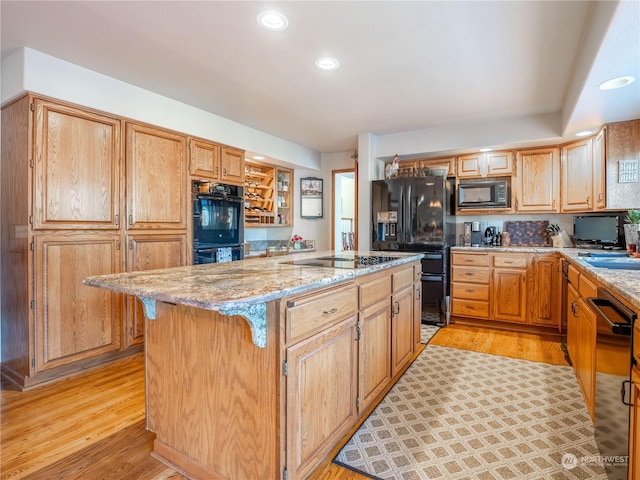 kitchen featuring light stone counters, black appliances, a center island, and light wood-type flooring