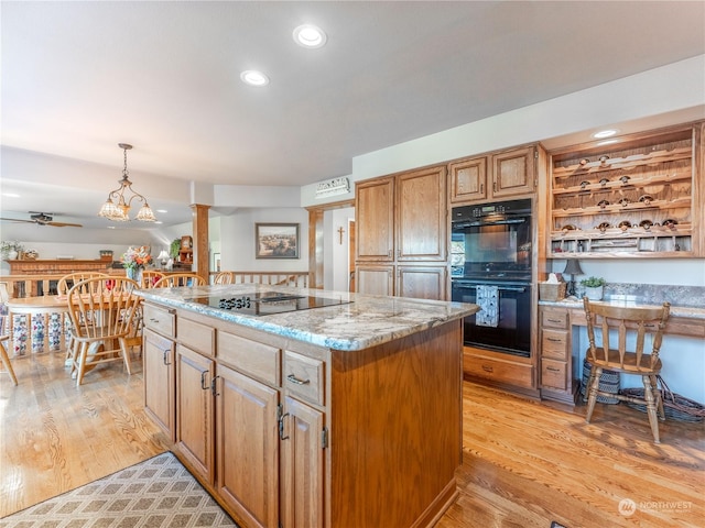 kitchen featuring light stone counters, a center island, light hardwood / wood-style flooring, pendant lighting, and black appliances