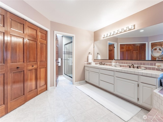 bathroom with a shower with door, vanity, tasteful backsplash, and tile patterned floors