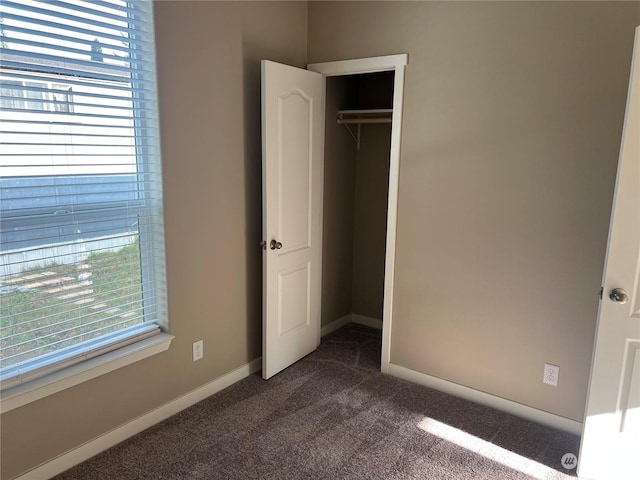 unfurnished bedroom with dark carpet and a closet