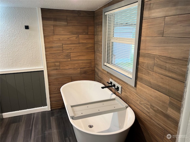 bathroom with sink, wood-type flooring, a textured ceiling, wooden walls, and a bathtub