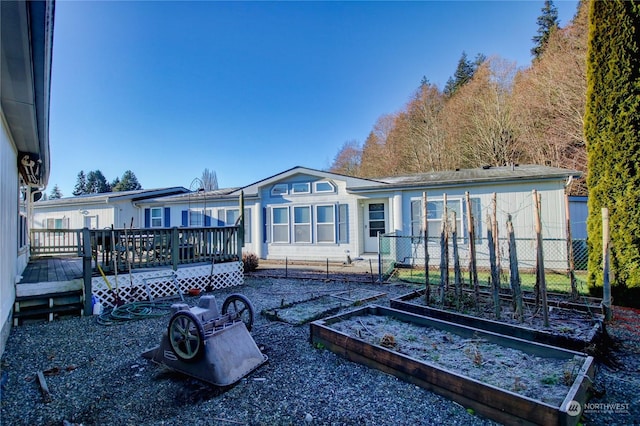 rear view of house with a deck, fence, and a garden