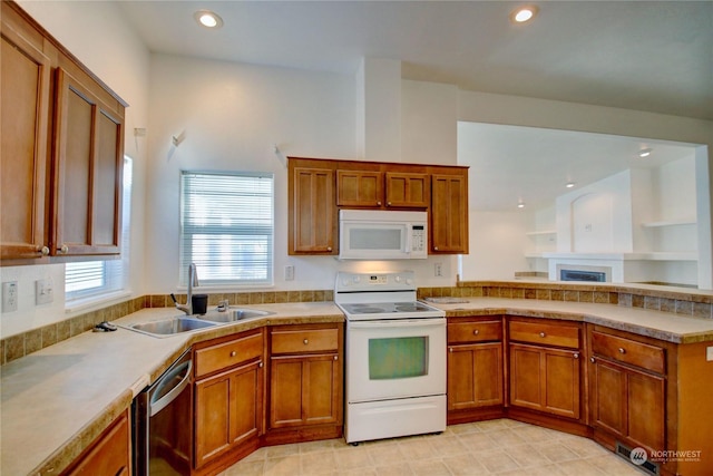 kitchen featuring recessed lighting, light countertops, brown cabinetry, a sink, and white appliances